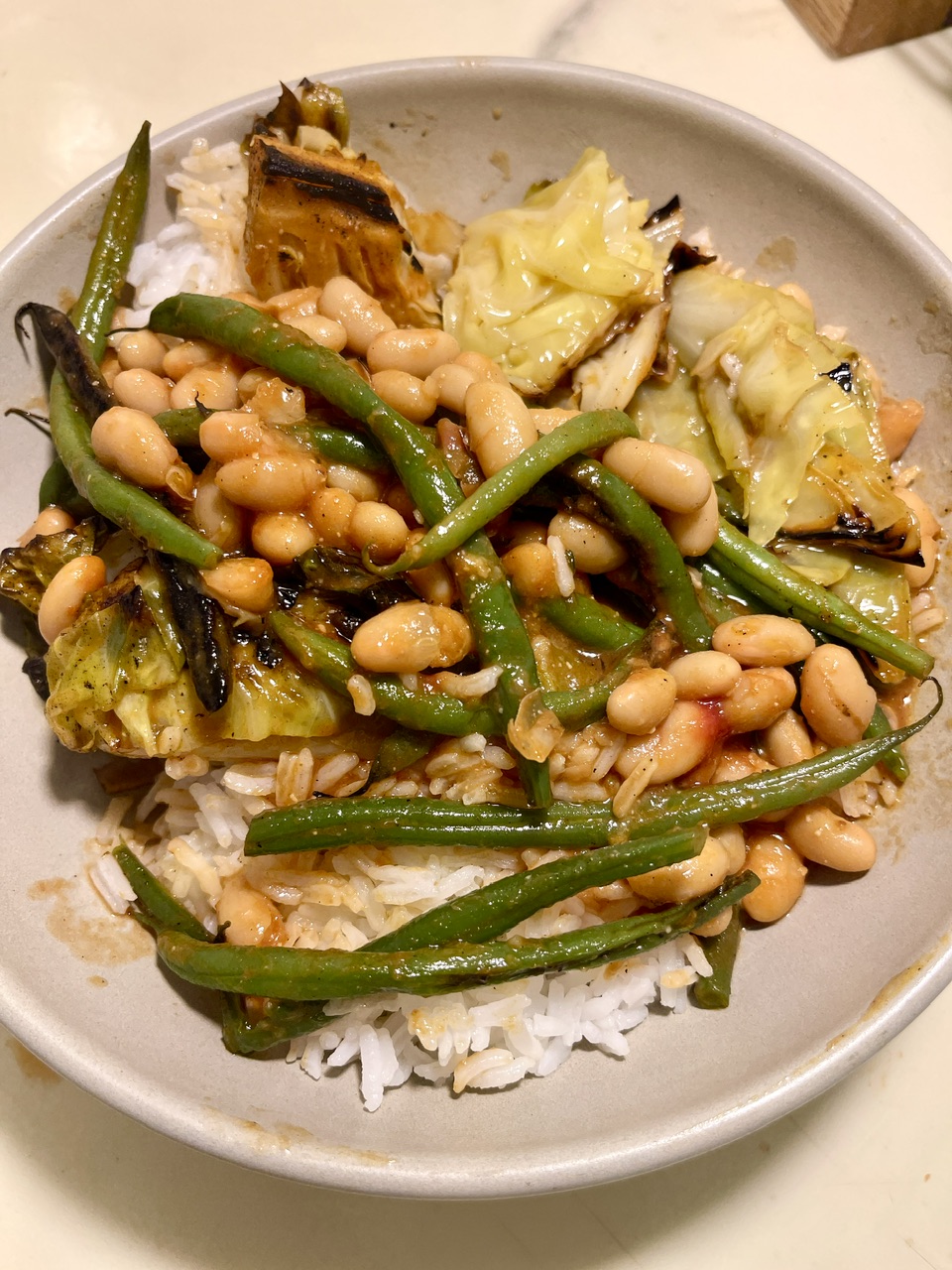 Braised hispi cabbage, green beans, and white beans over white rice in a bowl.
