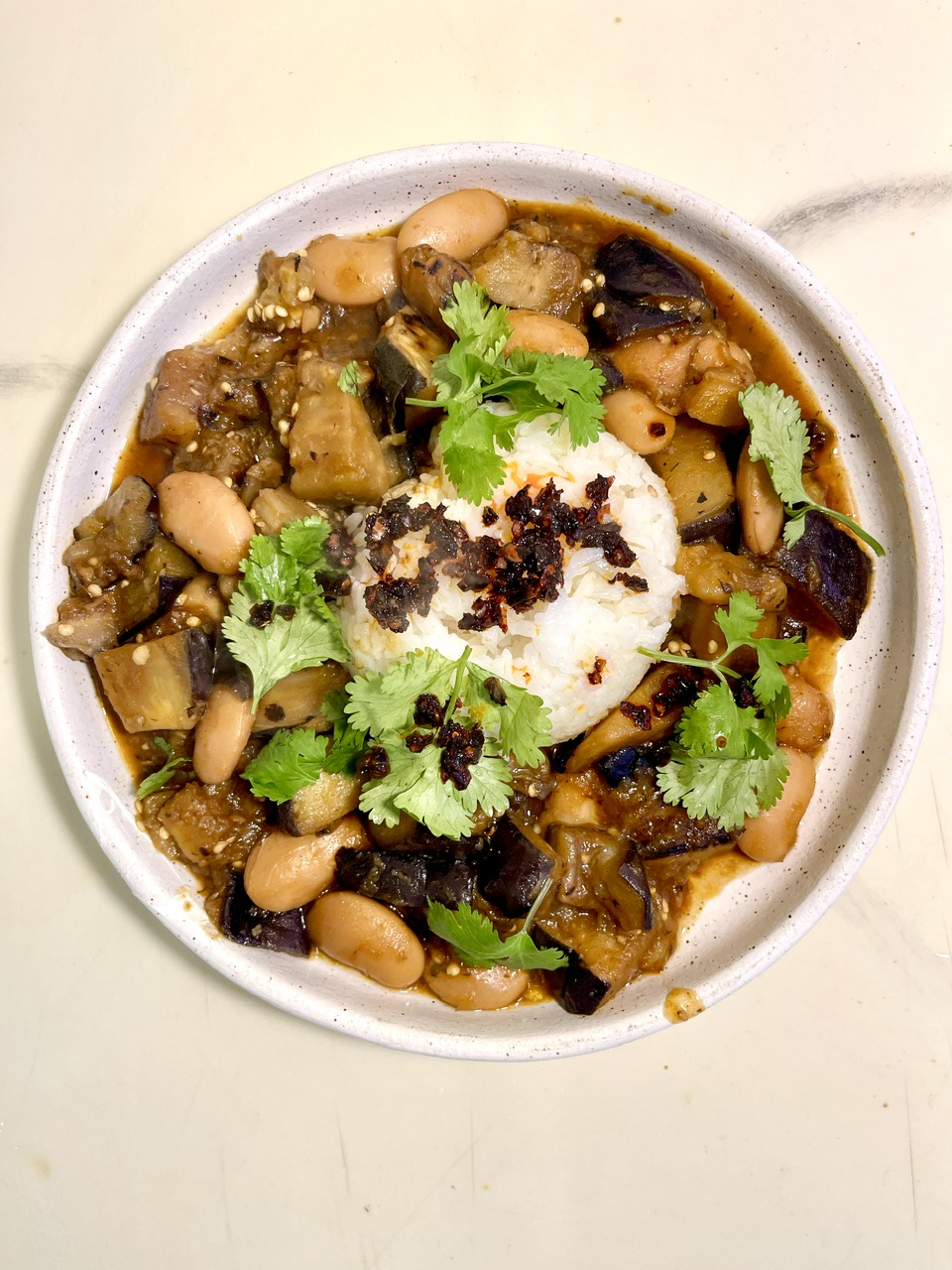 Caramelized eggplant with beans and cilantro over rice in a bowl.