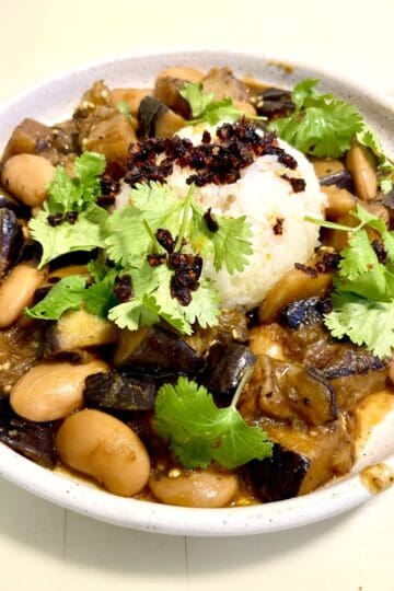 Caramelized eggplant with beans and herbs in a white bowl.