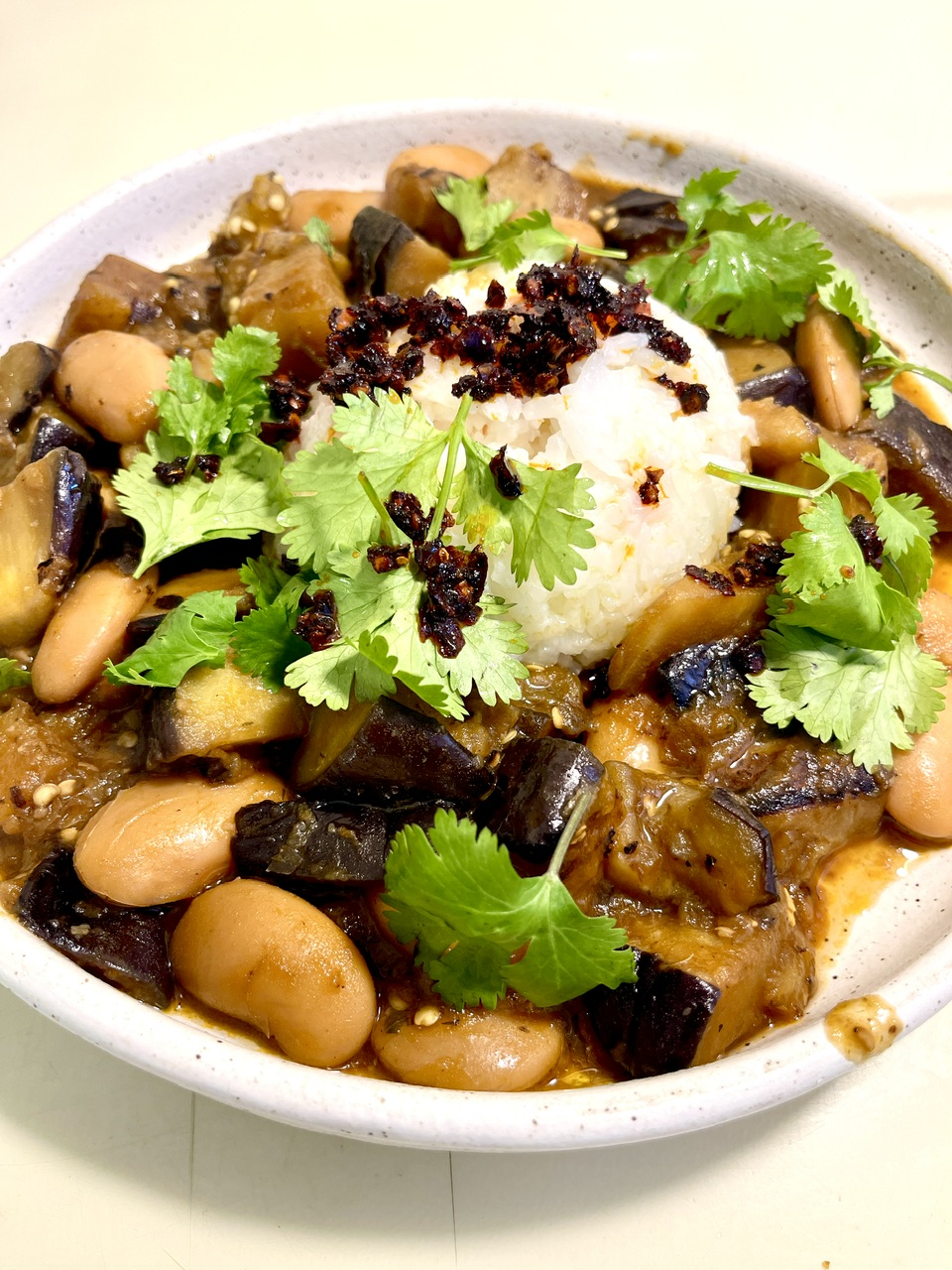Caramelized eggplant with beans and herbs in a white bowl.