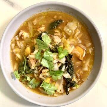 Smoky lentil soup with vegan sausage, sweet potato and herbs in a bowl.