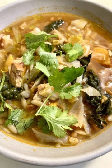 Hearty smoky harissa lentil soup with vegan sausage, sweet potato, orzo, and cilantro.