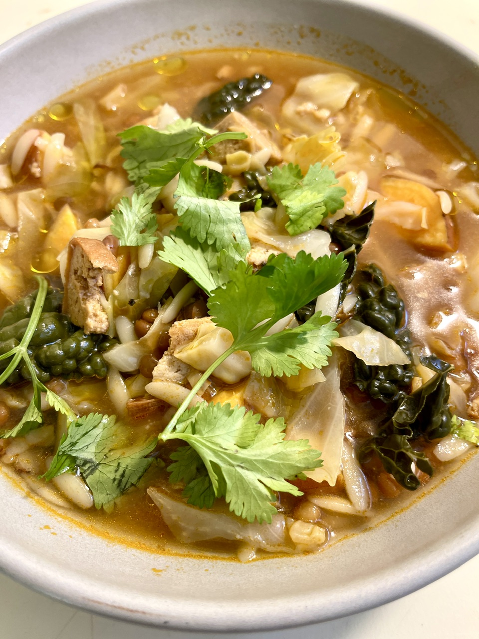 Hearty smoky harissa lentil soup with vegan sausage, sweet potato, orzo, and cilantro.