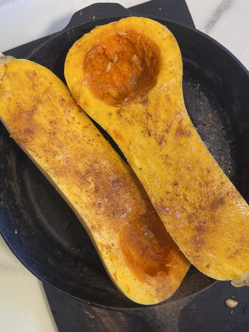 Roasted butternut squash halves with orange flesh on a dark plate.