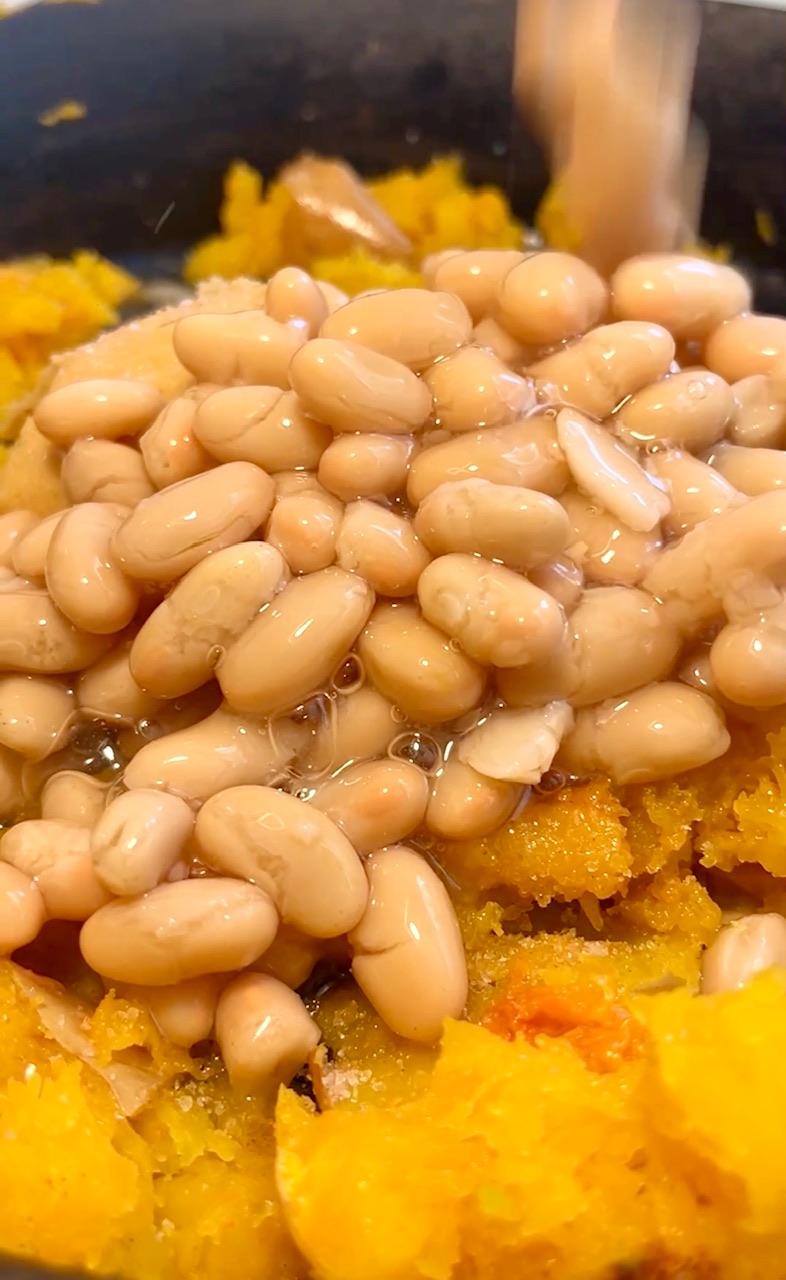 Creamy white beans over roasted butternut squash cubes in a pot.