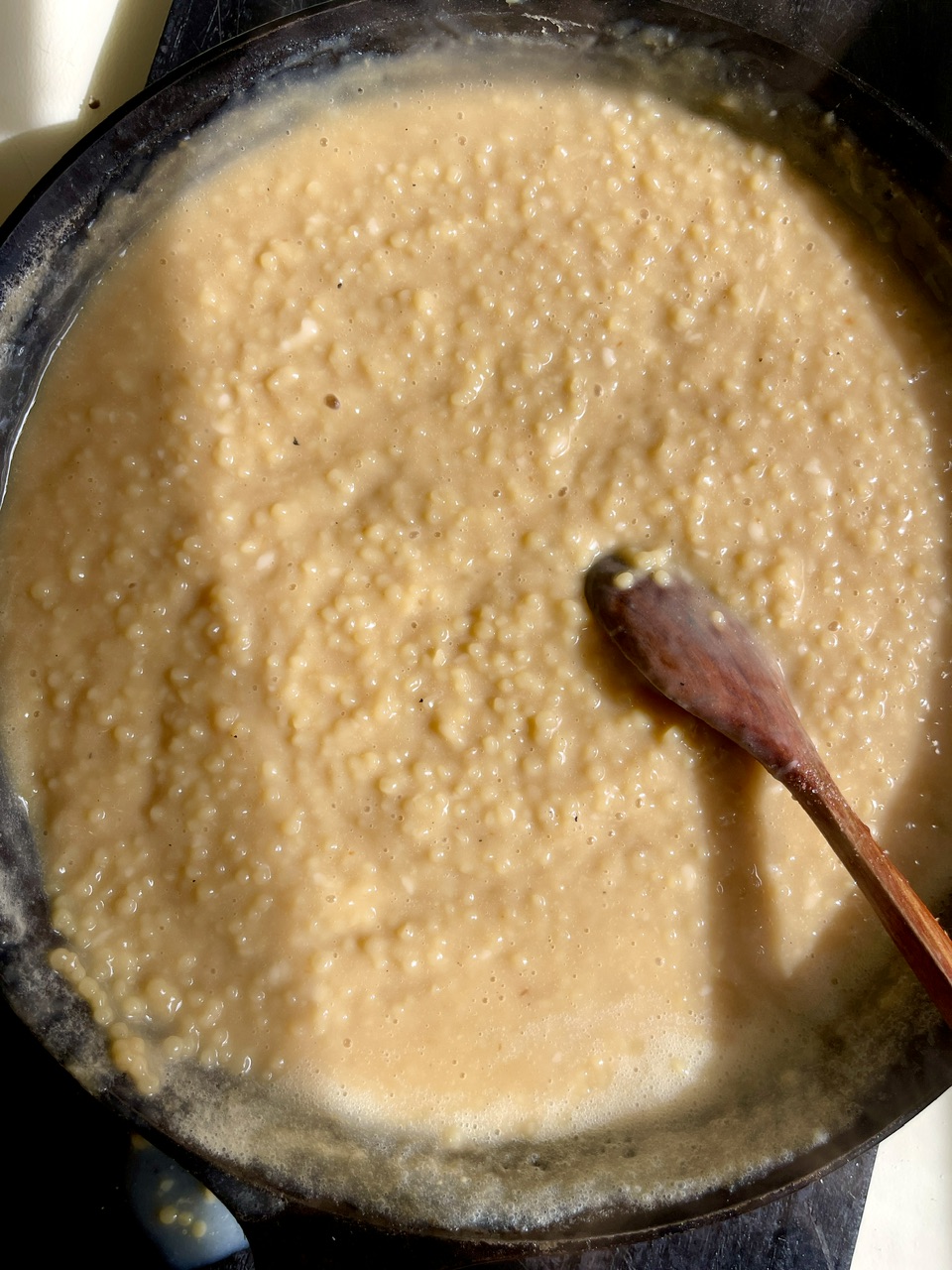Creamy vegan couscous risotto cooking in a pan with a wooden spoon.