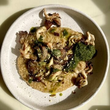 Creamy vegan couscous risotto with crispy mushrooms and pesto on a white plate.