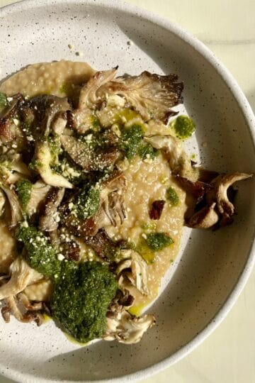 Creamy vegan couscous risotto with mushrooms and pesto in a white bowl.