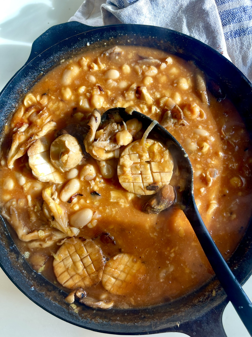 Hearty bean and oyster mushroom stew in a black skillet with a ladle.