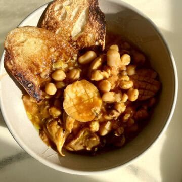 Hearty bean and mushroom stew with toasted bread slices in a white bowl.