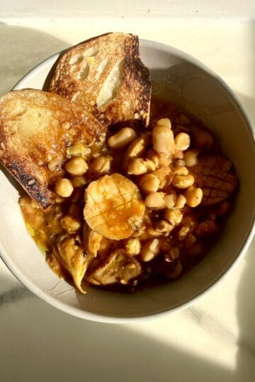 Hearty bean and mushroom stew with toasted bread slices in a white bowl.