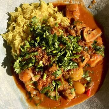 Vegan biryani served with crispy tofu and fresh herbs on a white plate.