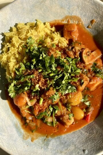 Vegan biryani served with crispy tofu and fresh herbs on a white plate.