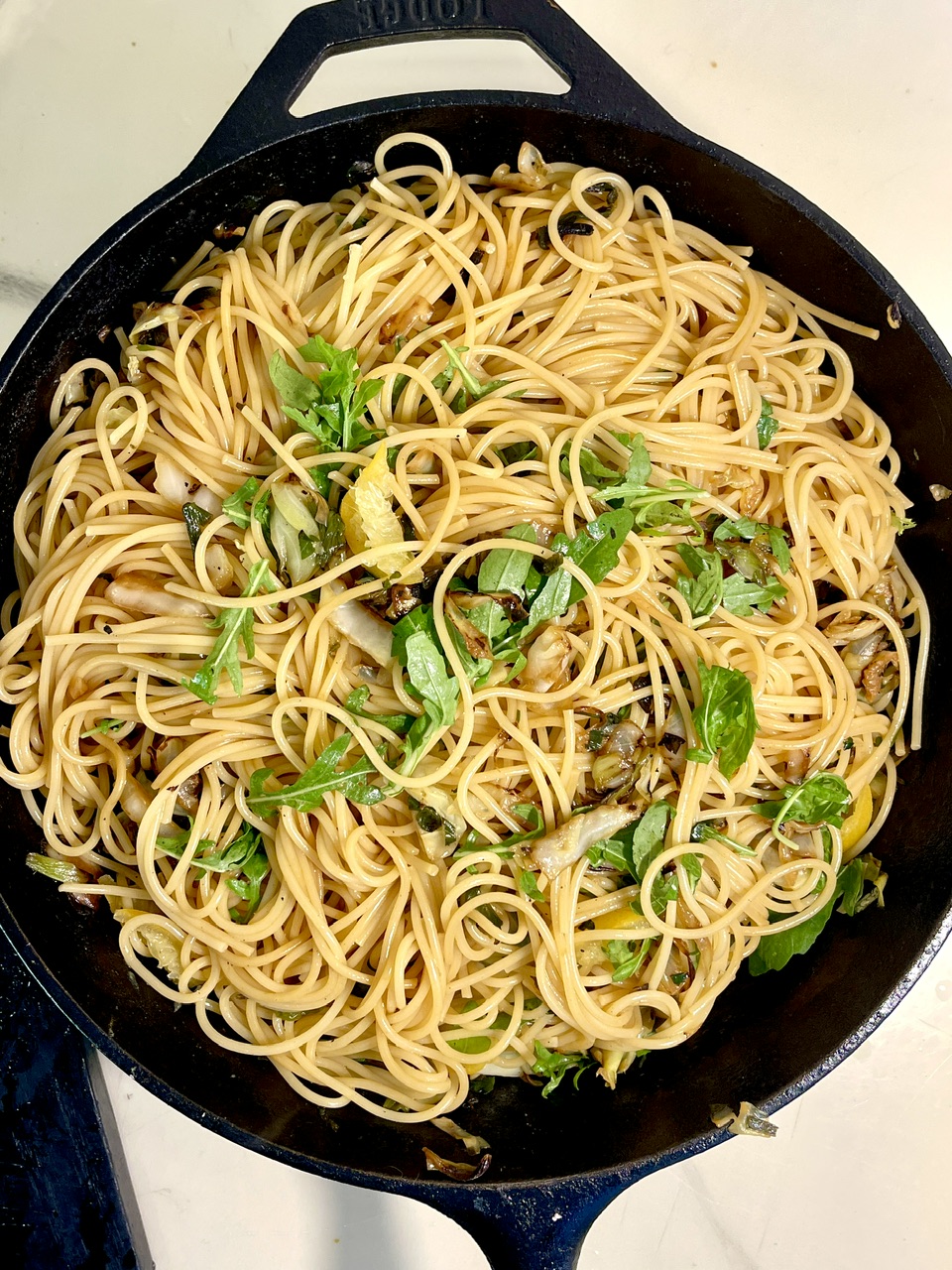 Delicious caramelized cabbage spaghetti with lemon and arugula in a skillet.