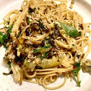 Close-up of caramelized cabbage spaghetti with lemon and herbs on a white plate.