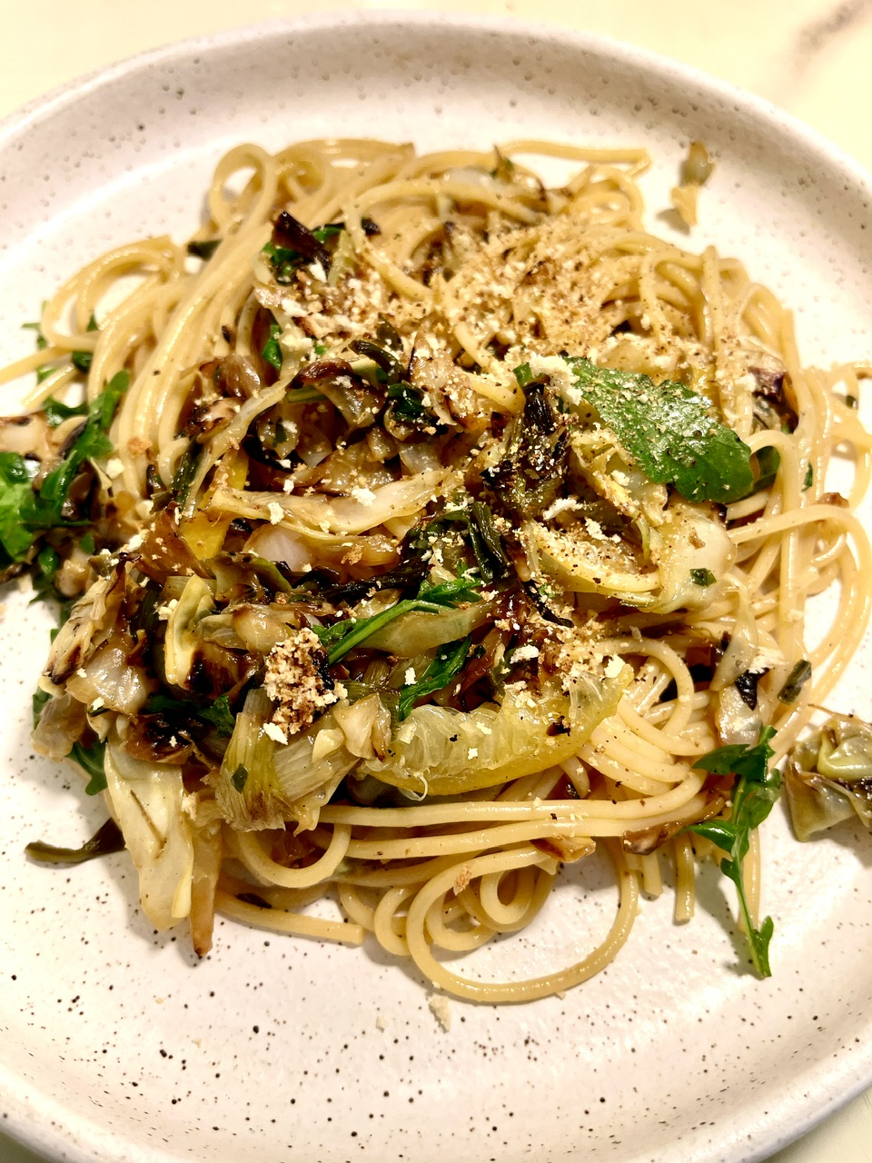 Close-up of caramelized cabbage spaghetti with lemon and herbs on a white plate.