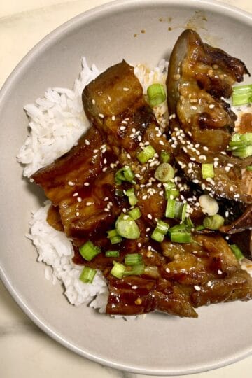 Vegan eggplant unagi served over rice with green onions and sesame seeds.