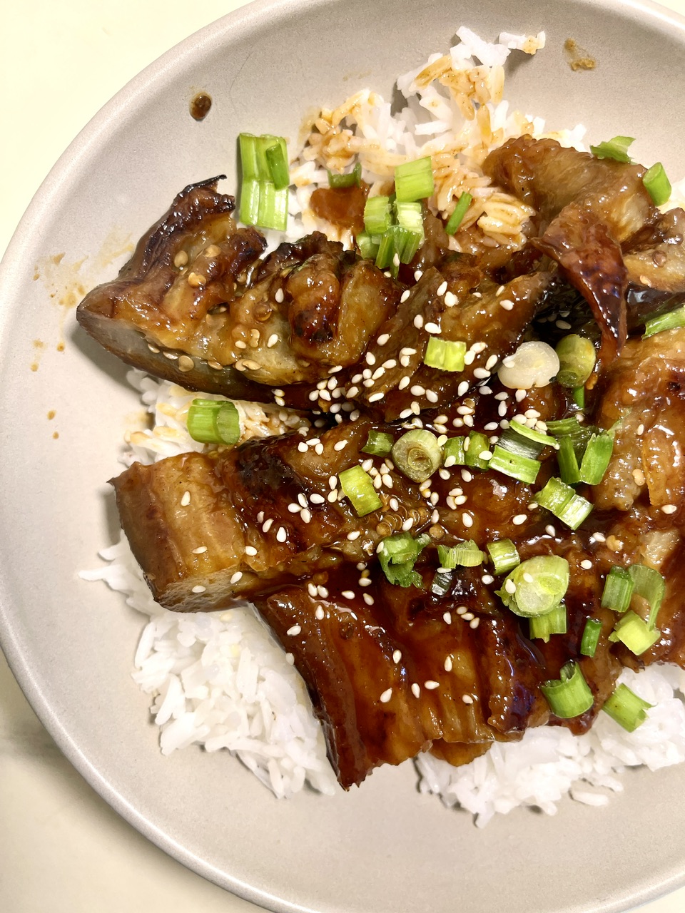 Vegan eggplant unagi served over rice with green onions and sesame seeds.