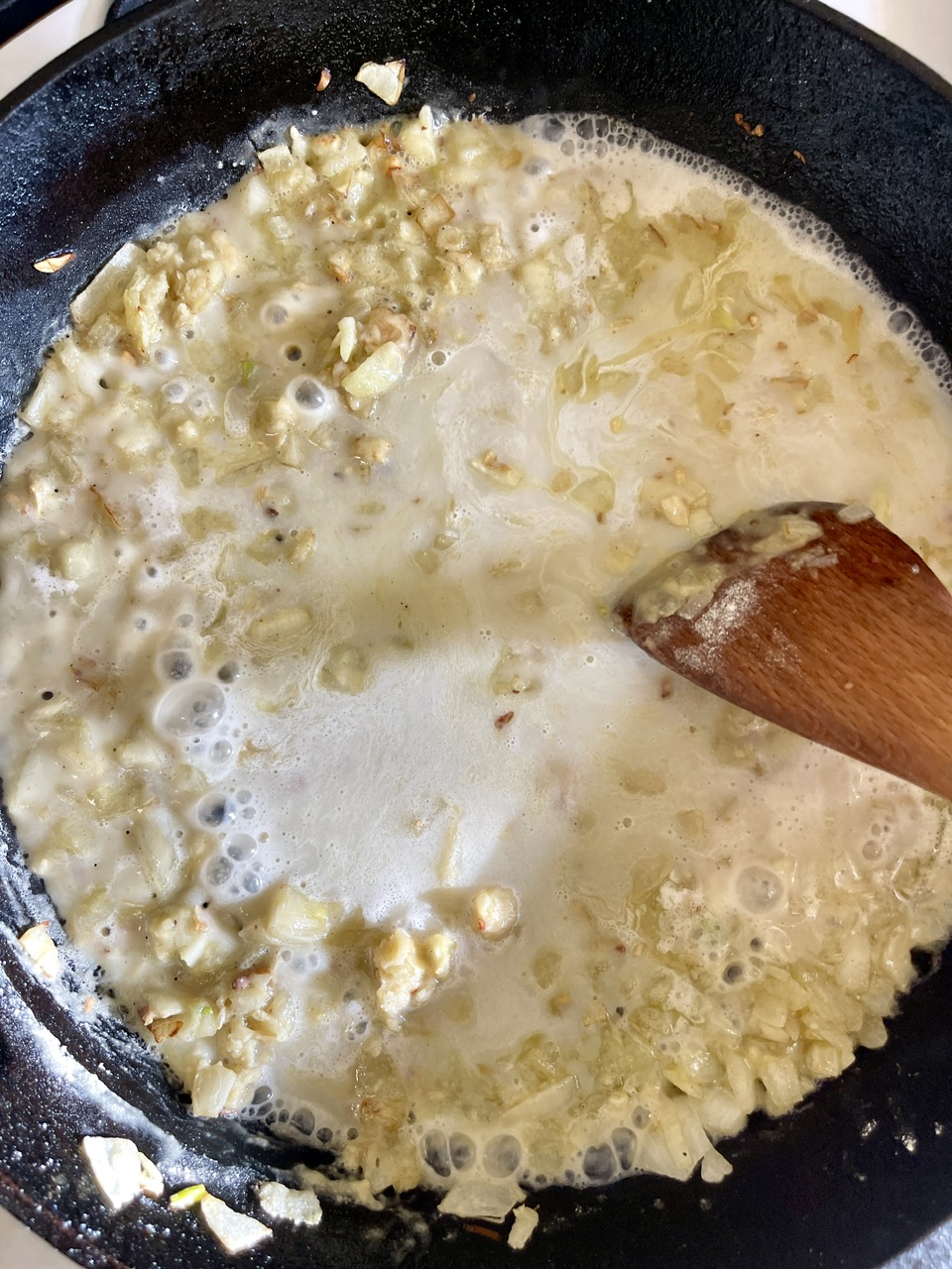 Creamy vegan garlic sauce simmering in a pan with garlic pieces.