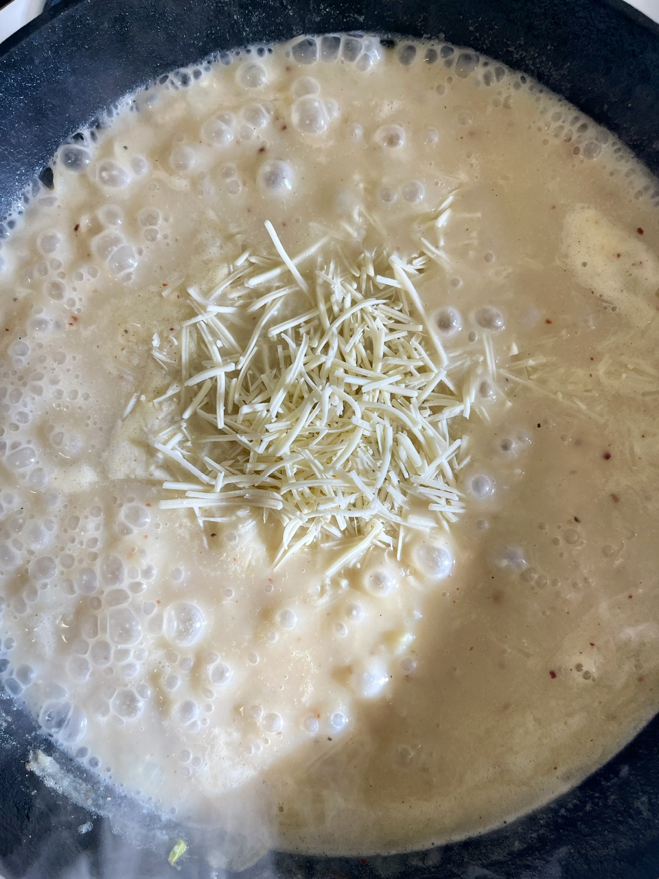 Creamy vegan garlic linguine with shredded cheese in a pan.
