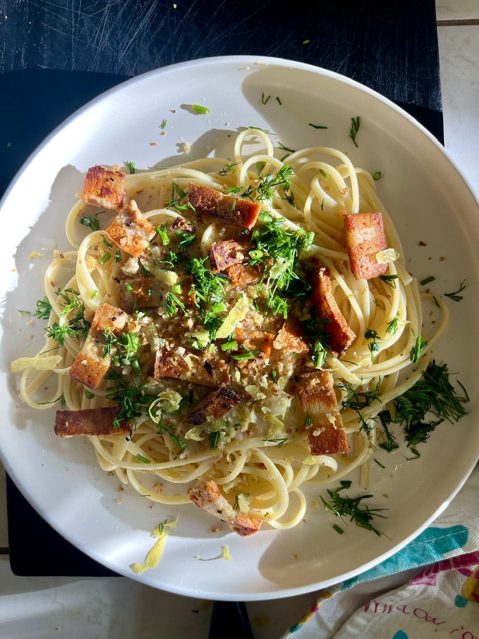 Vegan garlic linguine with crispy vegan bacon and fresh herbs on a white plate.