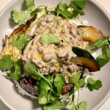 Vegan yogurt beans with seared vegetables and fresh cilantro on a white plate.