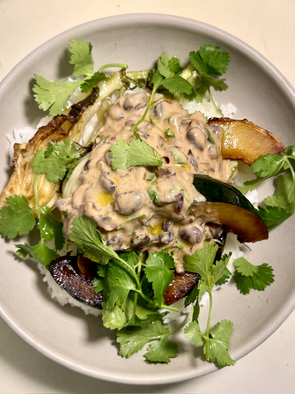 Vegan yogurt beans with seared vegetables and fresh cilantro on a white plate.