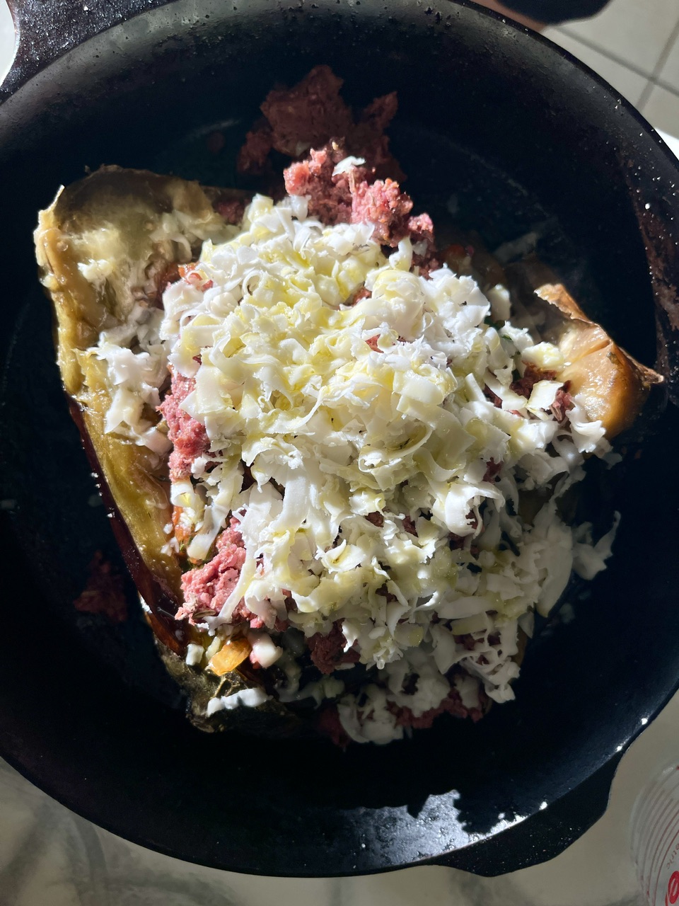 Vegan stuffed eggplant with cheese, tomatoes, and onions in a black skillet.