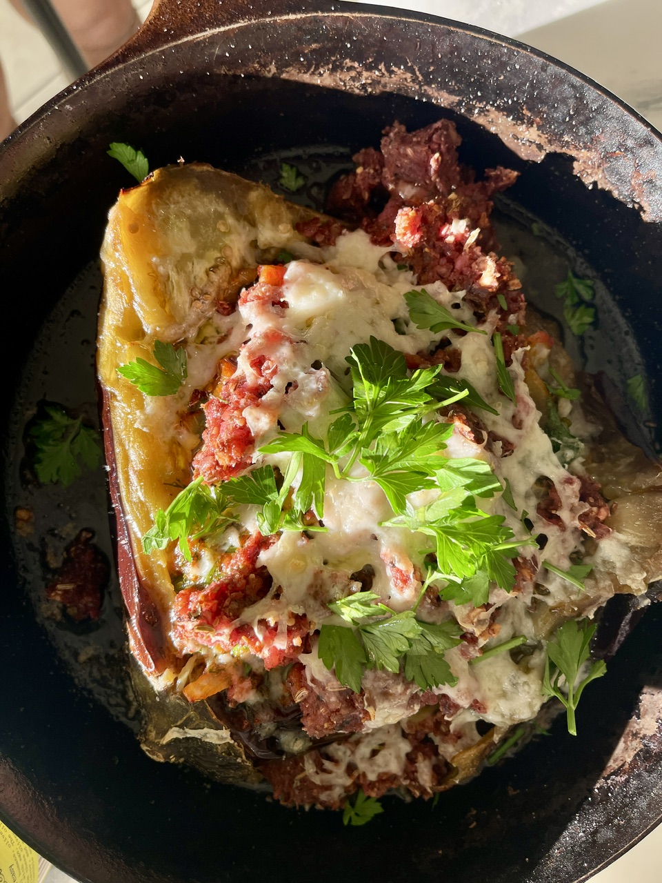 Baked eggplant stuffed with tomatoes, onions, and herbs in a skillet.