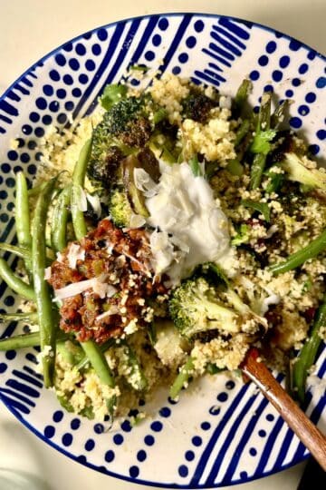 Mediterranean couscous with seared green beans and broccoli on a decorative plate.