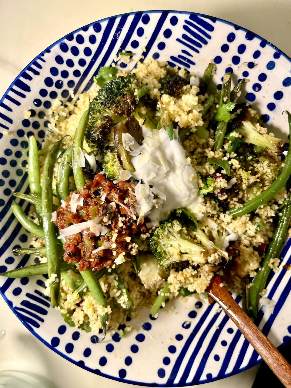 Mediterranean couscous with seared green beans and broccoli on a decorative plate.